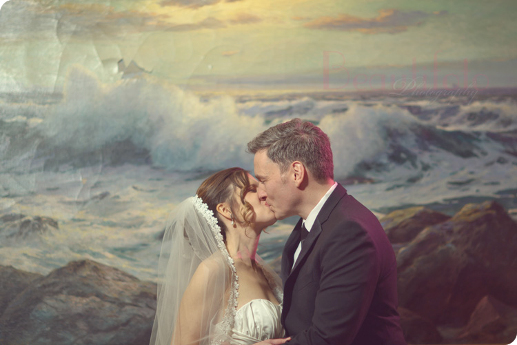Bride and groom's first kiss next to a painting of wave splash