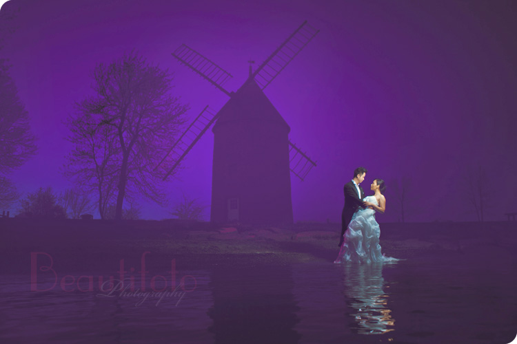 the bride and groom embrace in the water next to a wind mill at a trash the dress photo shoot in montreal