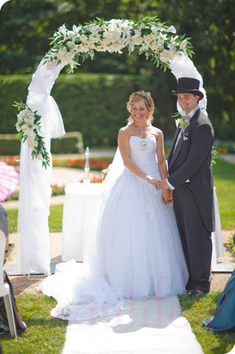 the bride and groom hold hands by a flower arch