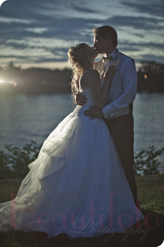 the bride and groom kissing by the river at sunset